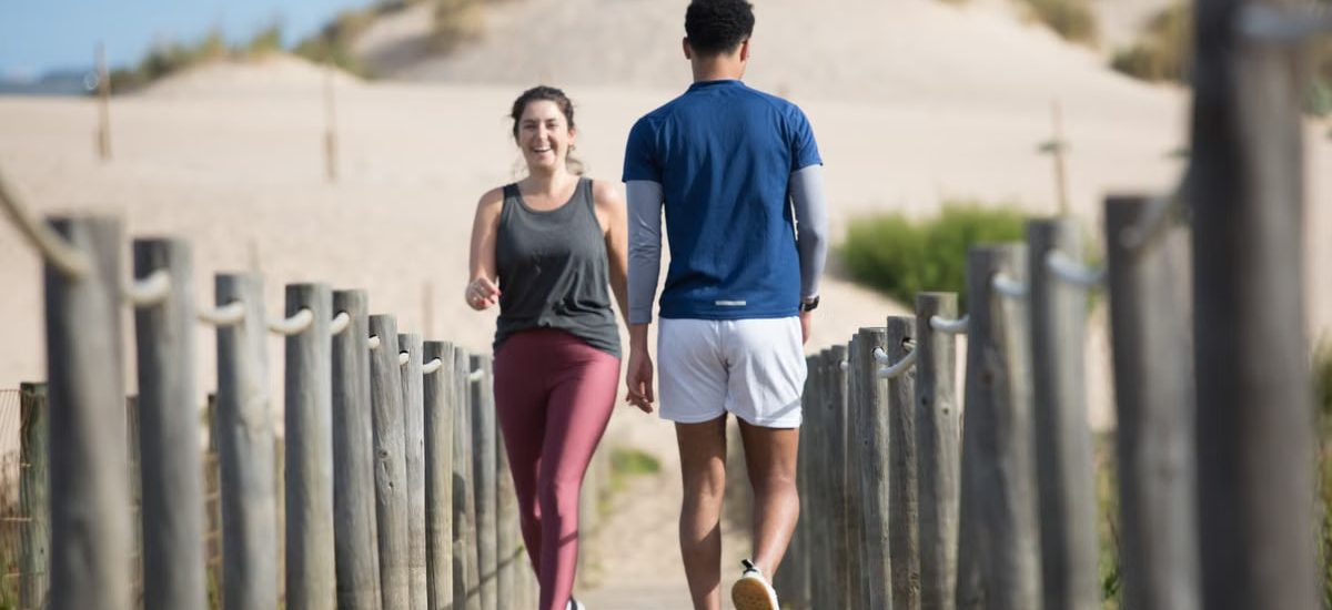 A couple enjoys jogging on a sunny beach boardwalk in Portugal, capturing a moment of fitness and leisure.