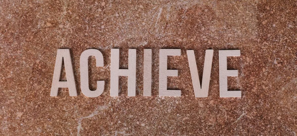 Wooden letters spelling 'ACHIEVE' on a textured brown surface, conveying motivation and success.