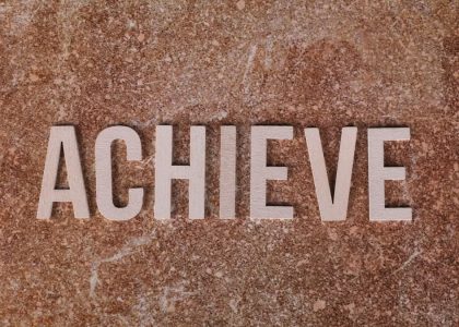 Wooden letters spelling 'ACHIEVE' on a textured brown surface, conveying motivation and success.